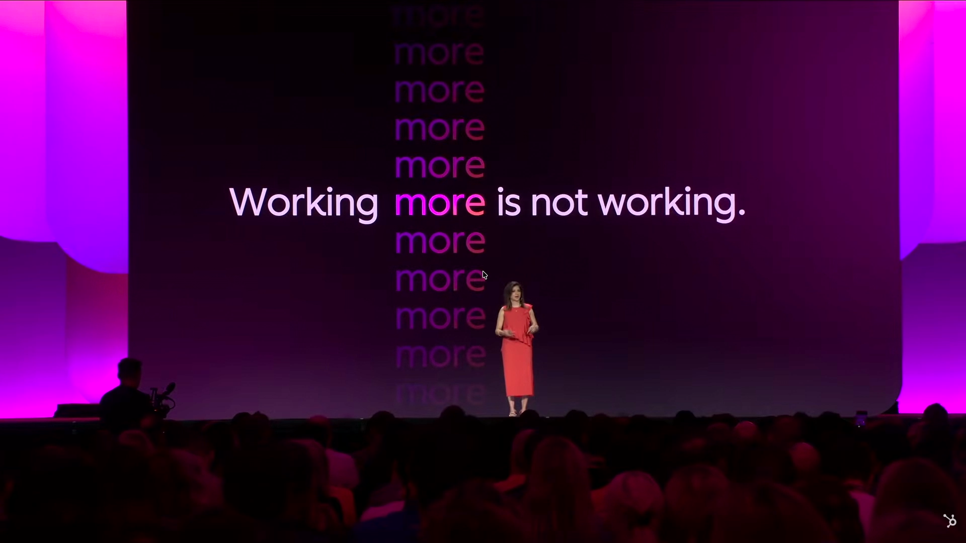 Presentation slide reading Working more is not working, with the speaker on stage