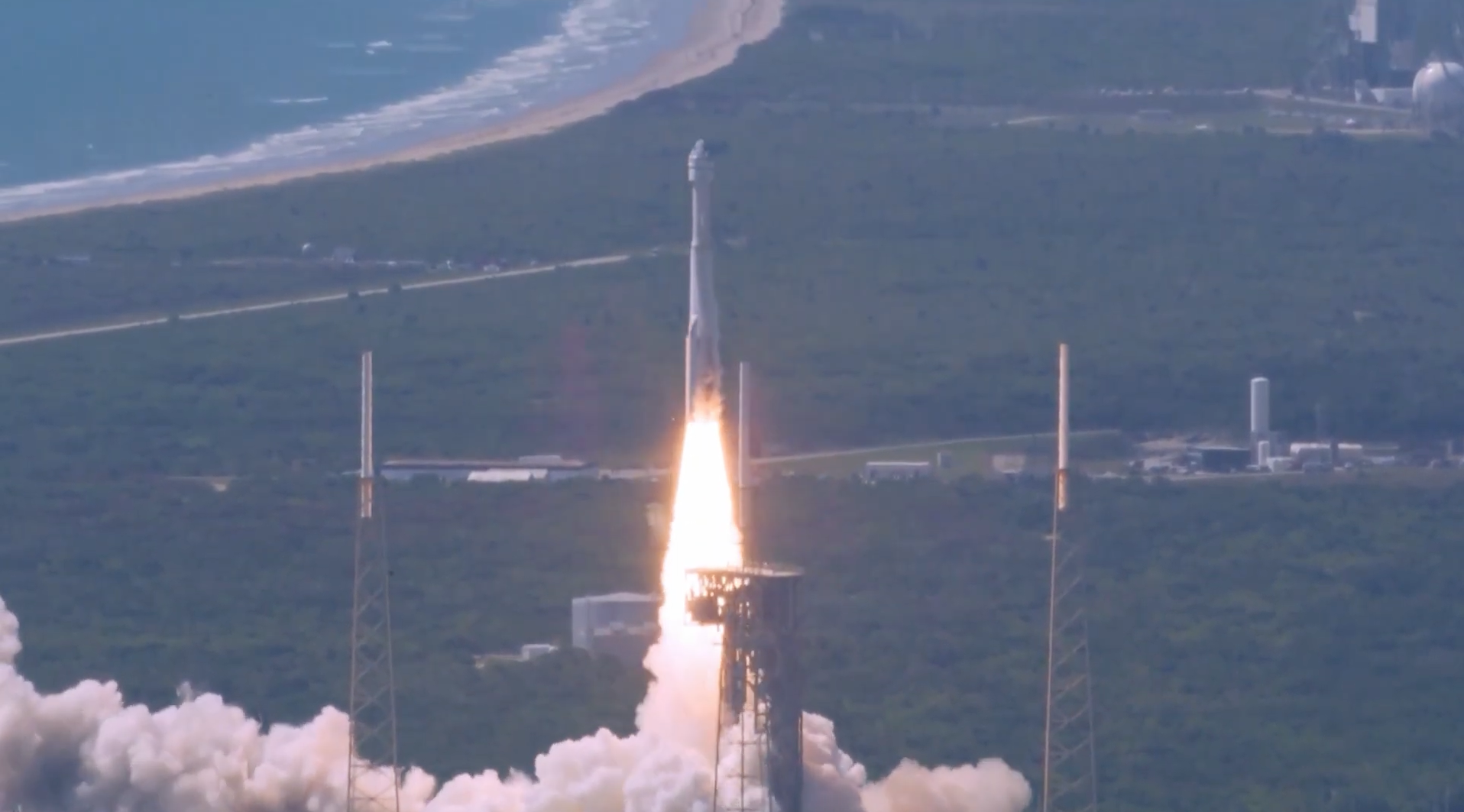 A rocket launching from a coastal launch pad, producing a bright plume of flame and a cloud of exhaust at liftoff