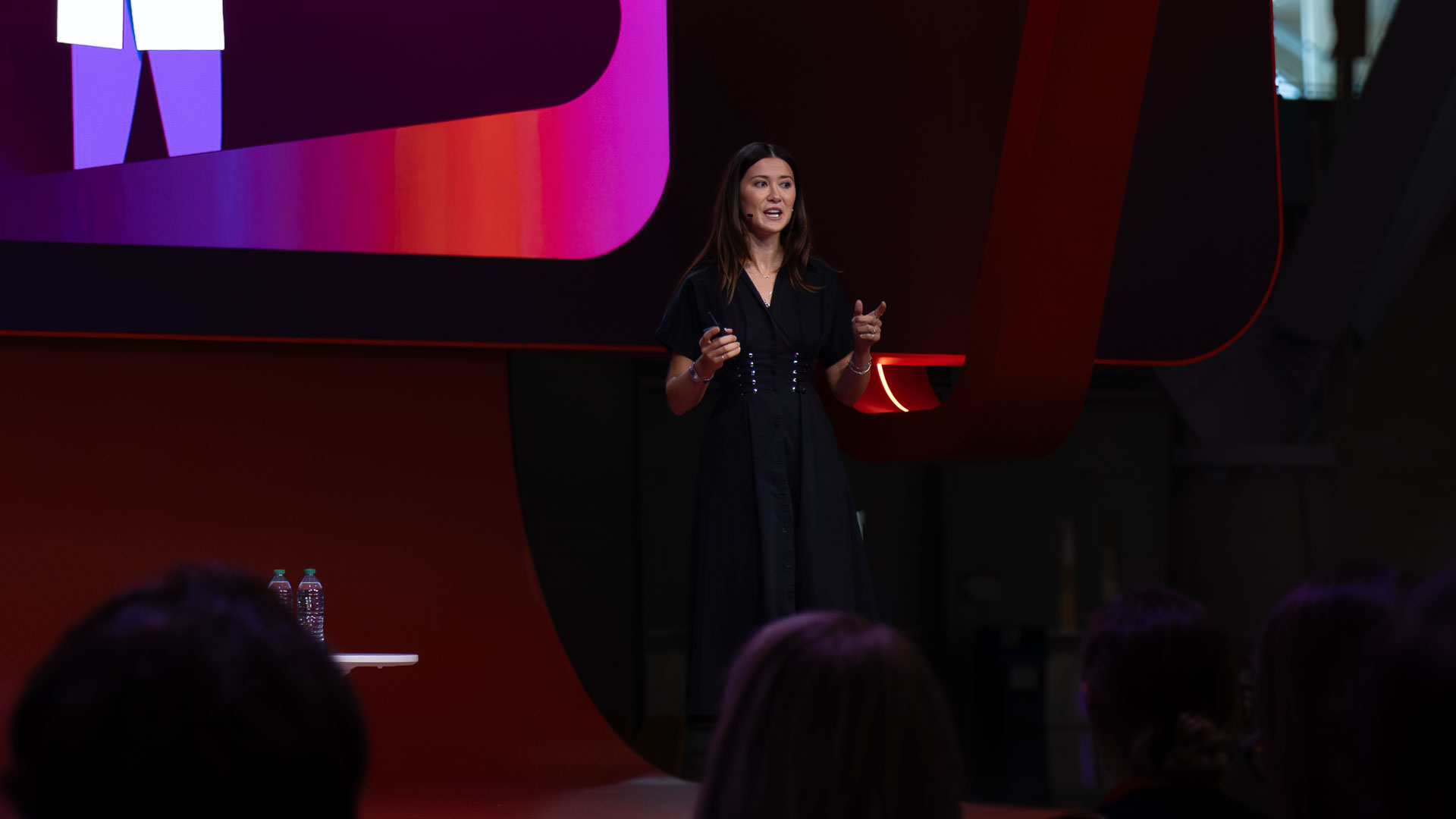 Amanda Copen presenting on stage in front of a large curved screen lit in pink and purple